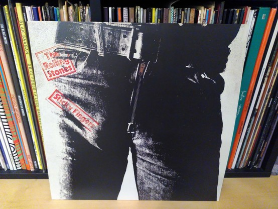 La copertina di Sticky Fingers dei Rolling Stones appoggiata ad altri vinili e su un ripiano di legno